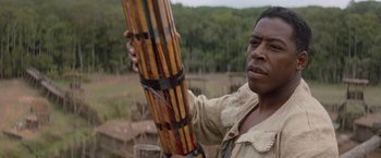 Movie still from “No Escape” (1994), directed by Martin Campbell – A man holding a wooden stick in his hand; Close Up shot, Low angle