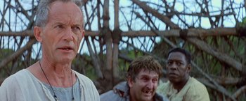 Movie still from “No Escape” (1994), directed by Martin Campbell – A group of men standing next to each other in front of a tree; Close Up shot, Low angle