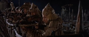 Movie still from “No Escape” (1994), directed by Martin Campbell – A group of men dressed in costumes and holding guns; Medium shot, Low angle