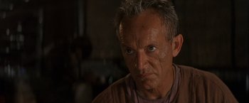 Movie still from “No Escape” (1994), directed by Martin Campbell – An older man with gray hair stares at the camera; Close Up shot, Over the shoulder angle