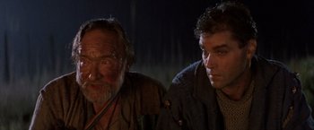 Movie still from “No Escape” (1994), directed by Martin Campbell – Two men sitting next to each other in the dark; Close Up shot, Over the shoulder angle