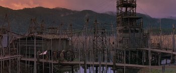 Movie still from “No Escape” (1994), directed by Martin Campbell – A man standing on a dock near a body of water; Extreme Wide shot, Low angle