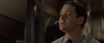 Movie still from “No Escape” (1994), directed by Martin Campbell – A man smoking a cigarette while wearing a shirt and tie; Close Up shot, Low angle