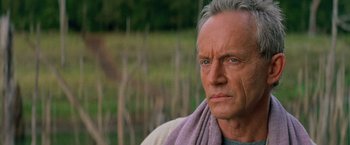 Movie still from “No Escape” (1994), directed by Martin Campbell – An older man with a towel around his neck; Close Up shot, Low angle