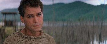 Movie still from “No Escape” (1994), directed by Martin Campbell – A person wearing a sweater near a body of water; Close Up shot, Over the shoulder angle