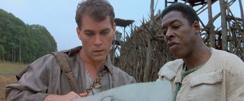 Movie still from “No Escape” (1994), directed by Martin Campbell – A man looking down at a piece of paper in front of another man; Close Up shot, Over the shoulder angle