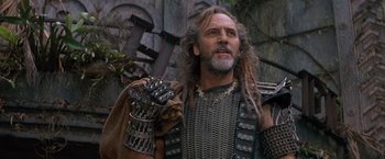 Movie still from “No Escape” (1994), directed by Martin Campbell – A man with long hair and a beard is wearing armor and holding a sword; Close Up shot, Low angle