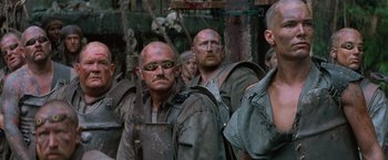 Movie still from “No Escape” (1994), directed by Martin Campbell – A group of men standing next to each other in the woods; Close Up shot, Low angle