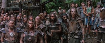 Movie still from “No Escape” (1994), directed by Martin Campbell – A group of men in the woods dressed as dwarves; Wide shot, High angle