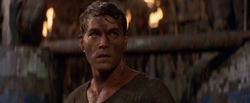 Movie still from “No Escape” (1994), directed by Martin Campbell – A person wearing a shirt with mud all over his face; Close Up shot, Low angle