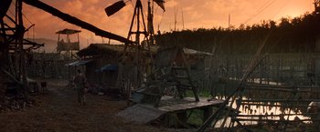 Movie still from “No Escape” (1994), directed by Martin Campbell – An old wooden structure in the middle of a field; Extreme Wide shot, Low angle