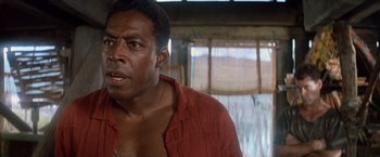 Movie still from “No Escape” (1994), directed by Martin Campbell – A person wearing a red shirt; Close Up shot, Low angle