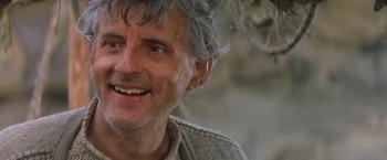 Movie still from “No Escape” (1994), directed by Martin Campbell – A person with grey hair smiling; Close Up shot, Low angle