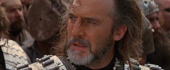 Movie still from “No Escape” (1994), directed by Martin Campbell – A person with long hair and a beard; Close Up shot, Over the shoulder angle