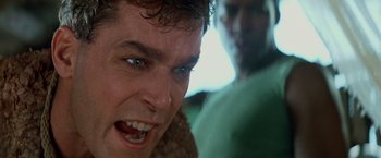 Movie still from “No Escape” (1994), directed by Martin Campbell – A man's face in a green shirt; Close Up shot, Low angle