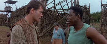 Movie still from “No Escape” (1994), directed by Martin Campbell – A group of men standing next to each other in a field; Close Up shot, Over the shoulder angle