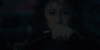 Movie still from “No Exit” (2022), directed by Damien Power – A woman sitting behind a steering wheel in a dark room; Close Up shot, Over the shoulder angle