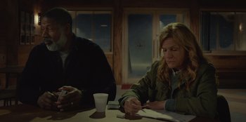 Movie still from “No Exit” (2022), directed by Damien Power – A man and a woman sitting at a table writing; Medium shot, High angle