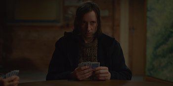 Movie still from “No Exit” (2022), directed by Damien Power – A man sitting at a table holding a deck of cards; Medium shot, Over the shoulder angle