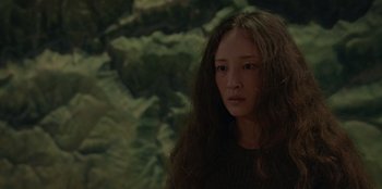 Movie still from “No Exit” (2022), directed by Damien Power – A woman with long brown hair standing in front of a forest; Close Up shot, High angle