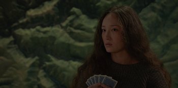 Movie still from “No Exit” (2022), directed by Damien Power – A young woman holding a bunch of playing cards in her hands; Close Up shot, Over the shoulder angle