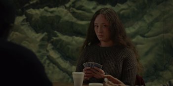 Movie still from “No Exit” (2022), directed by Damien Power – A woman sitting at a table holding a deck of playing cards; Medium shot, Over the shoulder angle