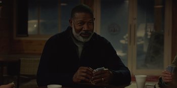 Movie still from “No Exit” (2022), directed by Damien Power – An older man sitting at a table holding a stack of money; Close Up shot, Over the shoulder angle