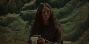 Movie still from “No Exit” (2022), directed by Damien Power – A woman sitting at a table with a cup of coffee in front of her; Medium shot, Over the shoulder angle