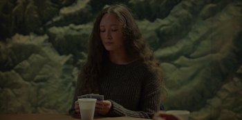 Movie still from “No Exit” (2022), directed by Damien Power – A woman sitting at a table with a cup of coffee in front of her; Close Up shot, Over the shoulder angle