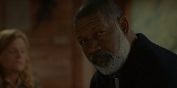 Movie still from “No Exit” (2022), directed by Damien Power – An older man with a gray beard looking at the camera; Close Up shot, Low angle