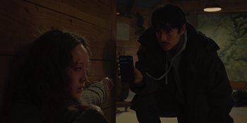 Movie still from “No Exit” (2022), directed by Damien Power – A man holding up a cell phone while another man looks on; Medium shot, Over the shoulder angle
