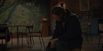 Movie still from “No Exit” (2022), directed by Damien Power – A man sitting on the ground in a room; Medium shot, High angle
