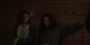 Movie still from “No Exit” (2022), directed by Damien Power – Two young girls sitting on a wooden wall; Medium shot, High angle