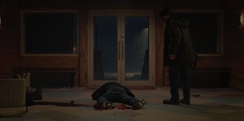 Movie still from “No Exit” (2022), directed by Damien Power – A man laying on the ground in front of a door; Wide shot, Over the shoulder angle