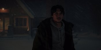 Movie still from “No Exit” (2022), directed by Damien Power – A man in a hooded jacket standing in the snow; Medium shot, Over the shoulder angle