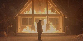 Movie still from “No Exit” (2022), directed by Damien Power – A man standing in front of a burning building; Wide shot, Over the shoulder angle