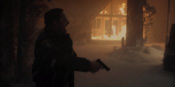 Movie still from “No Exit” (2022), directed by Damien Power – A man holding a gun in front of a burning house; Medium shot, Low angle