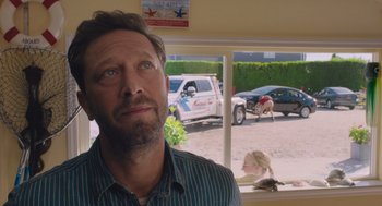 Movie still from “No Hard Feelings” (2023), directed by Gene Stupnitsky – A man standing in front of a window with a truck in the background; Close Up shot, Over the shoulder angle