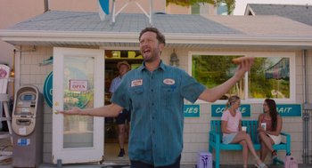 Movie still from “No Hard Feelings” (2023), directed by Gene Stupnitsky – A man standing in front of a store with his arms outstretched; Medium shot, Low angle