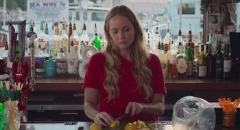 Movie still from “No Hard Feelings” (2023), directed by Gene Stupnitsky – A woman in a red shirt is cutting a lemon; Medium shot, Low angle