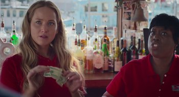 Movie still from “No Hard Feelings” (2023), directed by Gene Stupnitsky – A woman sitting in front of a bar holding a dollar bill; Close Up shot, Over the shoulder angle