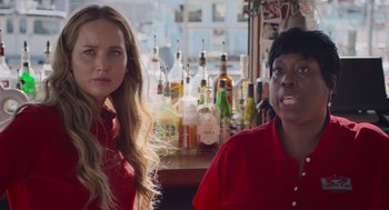 Movie still from “No Hard Feelings” (2023), directed by Gene Stupnitsky – Two women sitting in front of a bar with bottles of alcohol behind them; Close Up shot, Over the shoulder angle