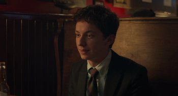 Movie still from “No Hard Feelings” (2023), directed by Gene Stupnitsky – A man in a suit and tie sitting in front of a wooden wall; Close Up shot, Over the shoulder angle