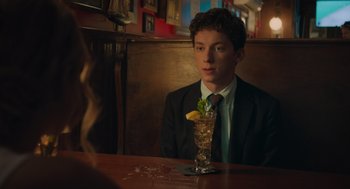 Movie still from “No Hard Feelings” (2023), directed by Gene Stupnitsky – A man sitting at a table with a drink in front of him; Medium shot, Over the shoulder angle