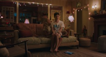 Movie still from “No Hard Feelings” (2023), directed by Gene Stupnitsky – A man and a woman sitting on a couch in a living room; Medium shot, Low angle