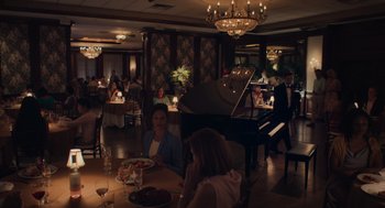 Movie still from “No Hard Feelings” (2023), directed by Gene Stupnitsky – People are sitting at a table in front of a grand piano; Wide shot, High angle