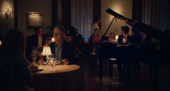Movie still from “No Hard Feelings” (2023), directed by Gene Stupnitsky – A man sitting at a table in front of a grand piano; Wide shot, Over the shoulder angle