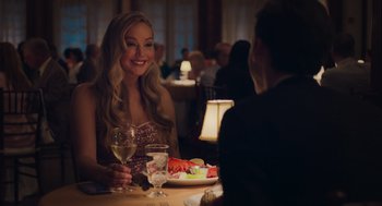 Movie still from “No Hard Feelings” (2023), directed by Gene Stupnitsky – A woman sitting at a dinner table with a glass of wine; Medium shot, Over the shoulder angle