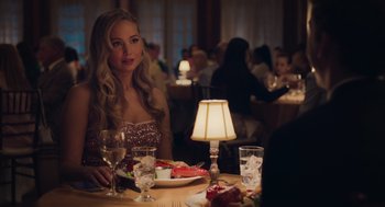 Movie still from “No Hard Feelings” (2023), directed by Gene Stupnitsky – A woman sitting at a table with a plate of food in front of her; Medium shot, Over the shoulder angle
