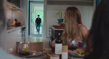 Movie still from “No Hard Feelings” (2023), directed by Gene Stupnitsky – A woman sitting at a dining room table looking at a man walking into a kitchen; Wide shot, Over the shoulder angle